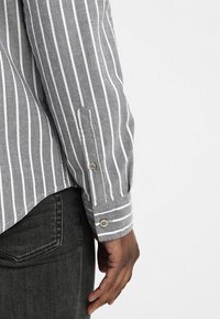 Camicia a strisce grigie con righe verticali bianche, maniche lunghe, polsini con bottoni e orlo curvo, realizzata in un tessuto testurizzato.