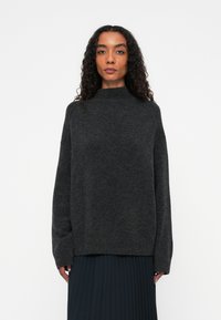 Ciemnoszary sweter z wysokim dekoltem, w oversize'owym fasonie i długimi rękawami. Posiada miękką strukturę, prążkowany dół i jest zestawiony z plisowaną spódnicą.