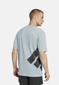 Camiseta deportiva de color azul claro con textura de malla, que presenta un gran diseño gráfico negro en la parte posterior, mangas cortas y un corte relajado.