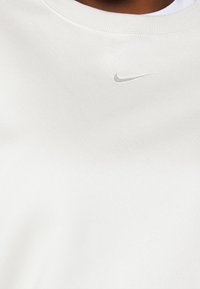 Vit sweatshirt med rund halsringning och ribbade muddar, med en liten, broderad silverfärgad Nike-logga på bröstet. Mjuk textur.