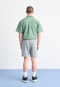 Grön kortärmad skjorta och grå träningsshorts. Skjortan har en avslappnad passform; shortsen har en bakficka och är gjorda av jerseytyg.
