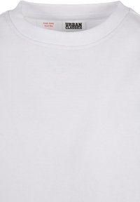 Närbild av vit Urban Classics t-shirt med rund hals med synlig etikett och säkerhetsvarning "Håll borta från eld."