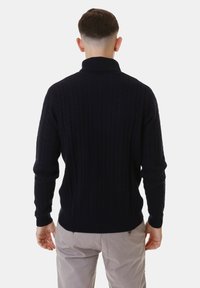 Maglione blu navy a treccia con colletto alto, dotato di polsini e orlo a coste. Realizzato in un materiale a maglia testurizzato per il calore.