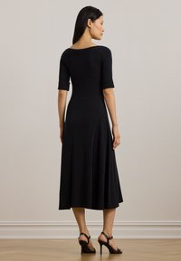 Fekete, testhez álló midi ruha rövid ujjal, kerek nyakkivágással és puha textúrával. Bőségben végződő szoknya jellemzi, fekete magassarkú szandálokkal párosítva.