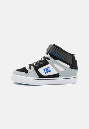 Zapatillas de media caña en gris, negro y blanco. Cuentan con cierre de cordones, detalle de correa y materiales texturizados con logotipo en el lateral.