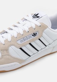 Vita läder- och beige mocka sneakers med svarta ränder, meshdetaljer och vita snören. Har den klassiska Adidas-logotypen på tungan.