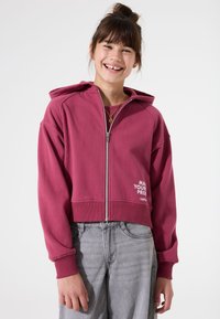 Sudadera corta con cremallera en color burdeos, con un acabado texturizado, bolsillo frontal y texto impreso "HAZ TU PROBLEMA" en blanco en el lado izquierdo.