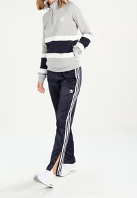 Ljust grå och marinblå randig idrottspullover med fjärdedelsdragkedja, kombinerad med marinblå träningsbyxor med vita sidostripes och ankelsprund.