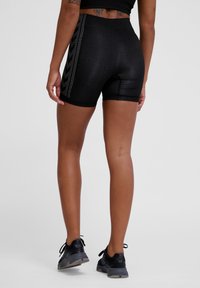Hoogwaardige zwarte sportshorts met een gestructureerde stof, voorzien van zijkanten met strepen en een strakke pasvorm, gecombineerd met zwarte sneakers.
