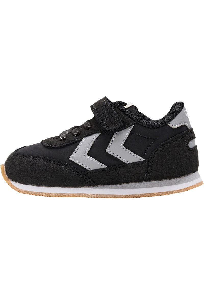 Sneaker nera con una fascia in velcro, design a chevron grigio, materiali in suede e tessuto, suola in gomma e dettagli color beige chiaro sul fondo.