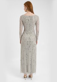 Lungo abito grigio da sera con elaborati dettagli in perline argento, maniche lunghe trasparenti e silhouette aderente, caratterizzato da un sottile design floreale.