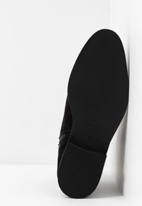 Sole di scarpa da uomo in suede nera con logo e indicazione della taglia 37, inclinata su uno sfondo bianco con angoli.