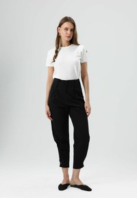 Witte korte mouw blouse, zwart hoogtailleurbroek met knopen bij de enkels, en zwarte slip-on schoenen; gladde texturen en een nauwsluitend ontwerp.