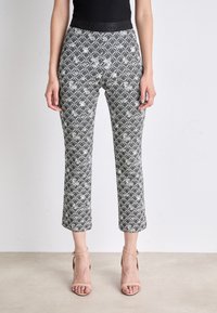 Schwarz-weiße gemusterte cropped Hose mit hexagonalem Design, ausgestattet mit einem glatten Bund. Getragen mit neutralen Riemchenschuhen.
