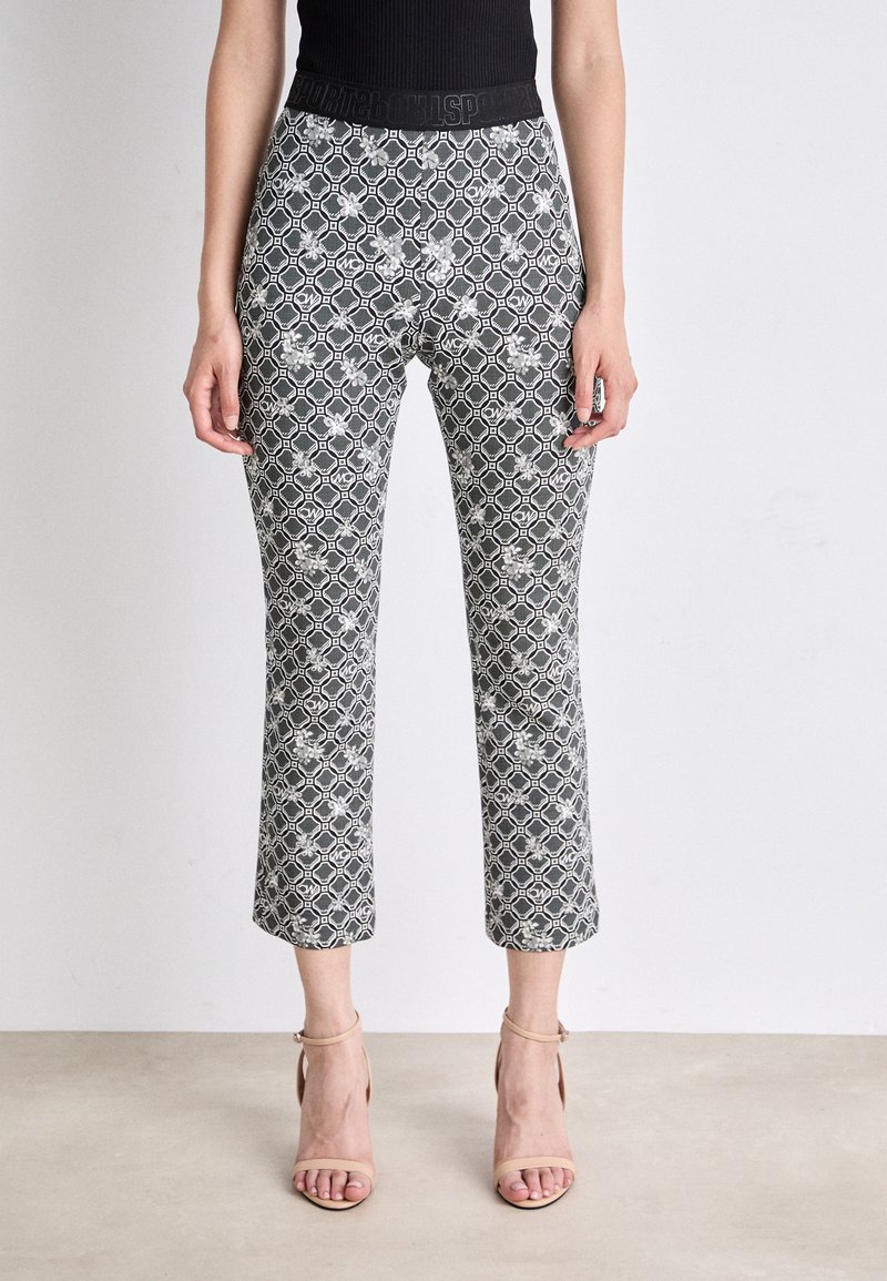 Schwarz-weiße gemusterte cropped Hose mit hexagonalem Design, ausgestattet mit einem glatten Bund. Getragen mit neutralen Riemchenschuhen.