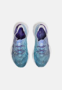 Zapatillas deportivas en degradado azul y púrpura con tejido texturizado, media suela blanca y cordones morados. Detalle de costura notable en la parte superior.