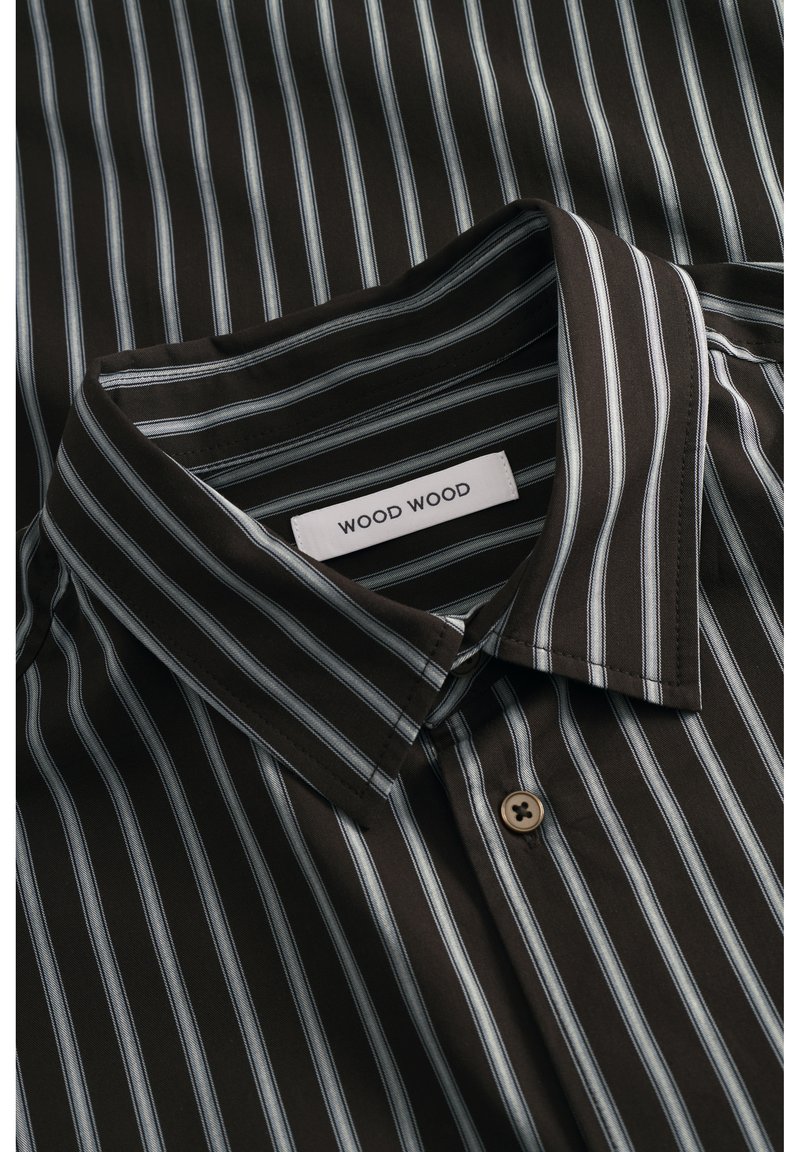 Chemise marron foncé avec des rayures verticales blanches et bleu clair, un col à boutons, et une étiquette de marque "WOOD WOOD" visible à l'intérieur du col.