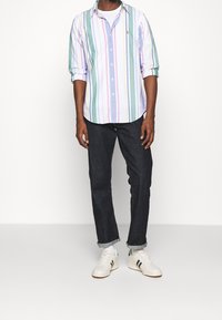 Camicia a righe in morbido cotone, caratterizzata da colori pastello, abbinata a jeans in denim scuro e scarpe bianche con accenti neri.