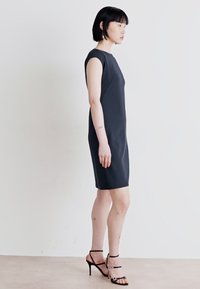 Black sleeveless dress with a fitted silhouette, knee-length hem, and smooth texture. Paired with black stiletto sandals featuring straps.