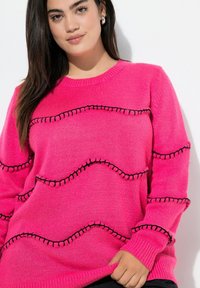 Suéter de punto rosa con un patrón de costura negra en ondas, cuello redondo y puños acanalados, con una textura suave y un ajuste relajado.