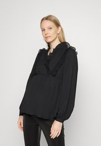Blusa preta feita de tecido leve, com um decote com babados, detalhes plissados e mangas bufantes longas. Estilizada com calças pretas justas.