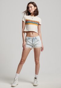 Beige cropped t-shirt met horizontale strepen in groen, oranje en blauw. Gecombineerd met lichte denim shorts met een kanten rand. Witte high-top sneakers.