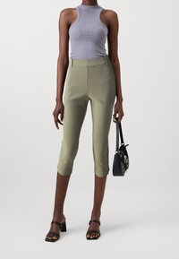 Svetle šedý žebrovaný top na ramínkách, olivové zkrácené kalhoty s přiléhavým střihem a černá kabelka. Modelka má na sobě černé sandály na podpatku.