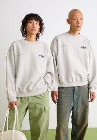Light gray oversized sweatshirts with front logos, paired with green cargo pants and blue jeans. Smooth fabric, relaxed fit, and casual style.