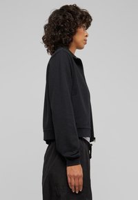 Svart kortärmad sweatshirt med en jämn textur, med hög krage och dragkedja. I kombination med löst sittande svarta byxor.
