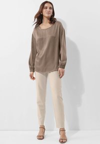 Braune, seidige Bluse mit langen Ärmeln, losem Schnitt und elastischen Bündchen, kombiniert mit hellbeigen Slim Pants und braunen Absatzsandalen.