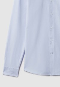 Svijetloplava košulja dugih rukava s gumbima, ravnim rubom i manžetama s jednim gumbom, prikazana sprijeda na svijetloj pozadini.