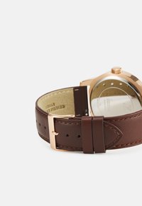 Brauner Lederuhrarmband mit einer goldfarbenen Edelstahl-Schnalle, das eine glatte Oberfläche und kontrastierende Nähte an den Kanten aufweist.