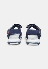 Tumesinine sandaalid Velcro rihmade ja valgete tallatega. Valmistatud pehmest materjalist, kontrastsete õmbluste ja punaste aktsentidega rihmadel.