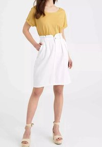 Yellow short-sleeve top paired with a high-waisted white skirt featuring a front button closure and pleated design; model wears beige wedge sandals.
