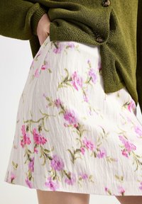 Blomstret mini nederdel i et cremet stof med pink og grønne blomstermønstre, sammen med en tekstureret olivengrøn sweater.