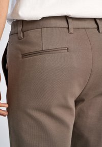 Bruine broek van textured stof, met een slim fit, riemlussen en een enkele paspelzak aan de achterkant.