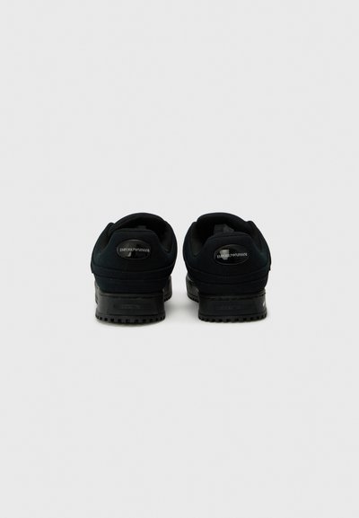 Black athletic shoes featuring a smooth fabric upper, textured accents, a cushioned collar, and a sturdy rubber sole with grip patterns.