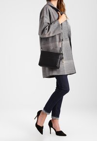 Black leather shoulder bag with a smooth texture, featuring a minimalist design and gold hardware accents, displayed beside a gray checkered coat.