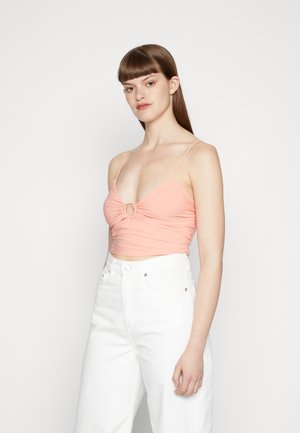 Top cropped rosa claro com um detalhe em corte redondo no centro, alças finas e tecido franzido, combinado com jeans brancos de cintura alta.