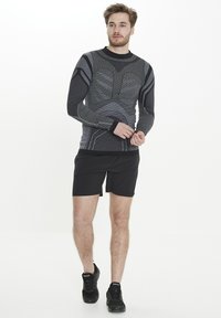 Långärmad svart och grå kompressionströja med texturerat mönster, atletisk passform, tillsammans med svarta shorts och svarta träningsskor.