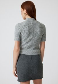 Lichtgrijze kabeltrui met korte mouwen, hoge hals en een textuurpatroon, gecombineerd met een donkergrijze hoge taille rok.