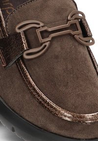 Mocasin de ante marrón con un acento de cuero brillante en marrón oscuro y una hebilla decorativa en forma de cadena en la correa. Superficie texturizada.