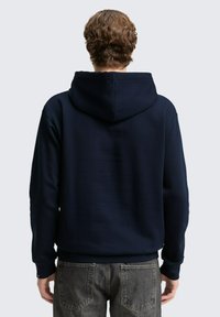 Marinblå hoodie med texturerad yta, justerbar huva och ribbad mudd. I kombination med grå jeans har den en avslappnad passform och enkel design.