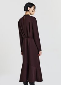 Langärmliges, braunes Kleid mit hohem Ausschnitt, elastischem Bund und schwingendem Saum. Verfügt über einen Schlüsselloch-Ausschnitt im Rücken für einen besonderen Akzent.