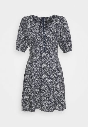 Robe florale bleu marine et blanche avec des manches courtes bouffantes, des boutons à l'avant, une taille ajustée et une jupe jusqu'aux genoux sur fond uni.