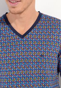 V-neck shirt in blue cotton with a multicolored zigzag pattern. Navy collar, small logo on the chest, short sleeves, and textured fabric.