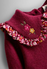 Pulover roz închis cu o textură ribbed, având un volan cu imprimeu floral și accente cu flori brodate aproape de guler.