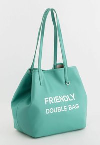 Teal-nahkainen kassi, jossa on kaksoiskahvat, ja teksturoitu pinta. Kassin etupuolella on valkoisella teksti "FRIENDLY DOUBLE BAG".
