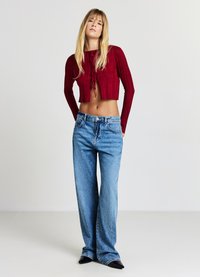 Roter, gerippter, kurz geschnittener Pullover mit vorderen Bindebändern, kombiniert mit taillierten, hellblauen Schlagjeans. Beide Kleidungsstücke zeichnen sich durch ein lässiges, entspanntes Design aus.