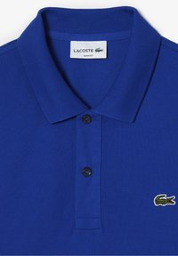 Modrý úzký polo tričko Lacoste s dvěma knoflíky, žebrovaným límečkem a vyšitým zeleným krokodýlem na hrudi.